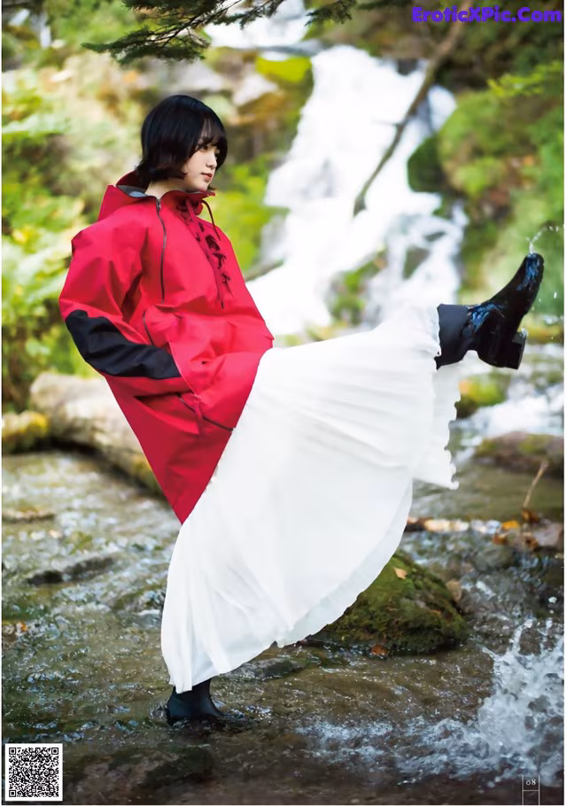 A woman in a red raincoat and white skirt standing in a stream.