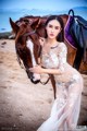 A woman in a white dress standing next to a brown horse.