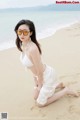 A woman in a white bikini sitting on the beach.