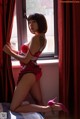 A woman in a red lingerie sitting on a window sill.