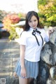 A woman in a school uniform leaning against a stone wall.