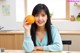 A woman sitting at a table holding an orange.