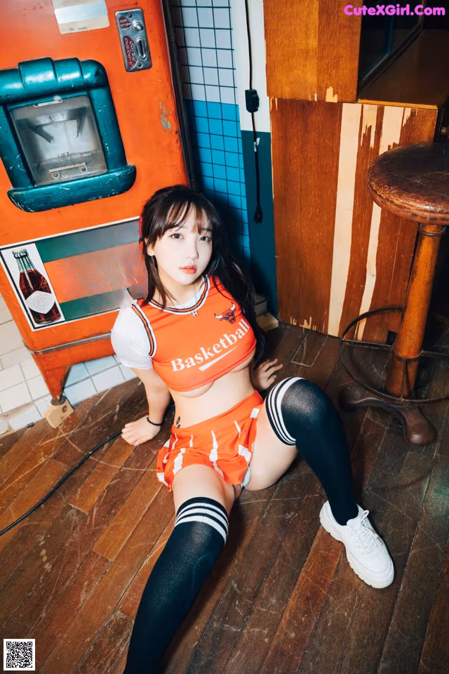 A woman sitting on the floor in front of a soda machine.