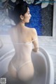 A woman in a white lingerie sitting in a bathtub.