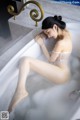 A woman in a white lingerie sitting in a bathtub.