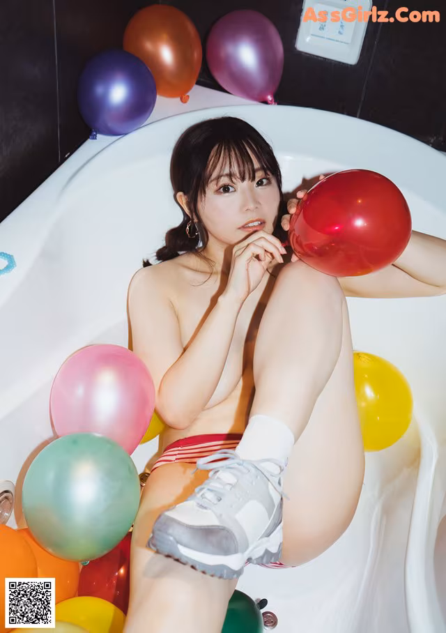 A woman sitting in a bathtub surrounded by balloons.