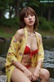 A woman in a yellow kimono sitting on a rock by the water.