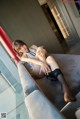 A woman sitting on top of a couch next to a window.