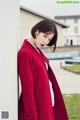 A woman in a red coat leaning against a wall.