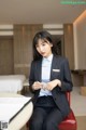 A woman in a business suit sitting on a red chair.