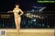 A woman in a bikini standing on a balcony at night.