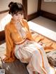 A woman in an orange and white kimono sitting on a bed.