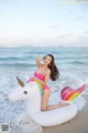 A woman in a pink bikini sitting on an inflatable unicorn on the beach.