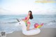 A woman in a bikini sitting on an inflatable unicorn on the beach.