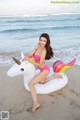 A woman in a pink bikini sitting on an inflatable unicorn on the beach.