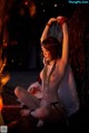 A naked woman sitting in front of a fire.