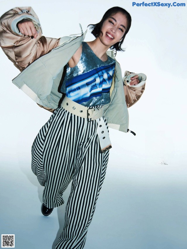 A woman in a blue top and striped pants posing for a magazine.