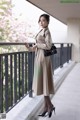 A woman in a beige coat is standing on a balcony.