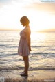 A woman in a pink dress standing on the beach at sunset.