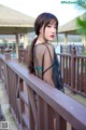 A woman in a sheer black dress standing on a wooden bridge.