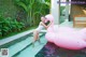 A woman in a white bathing suit standing next to a pink flamingo.